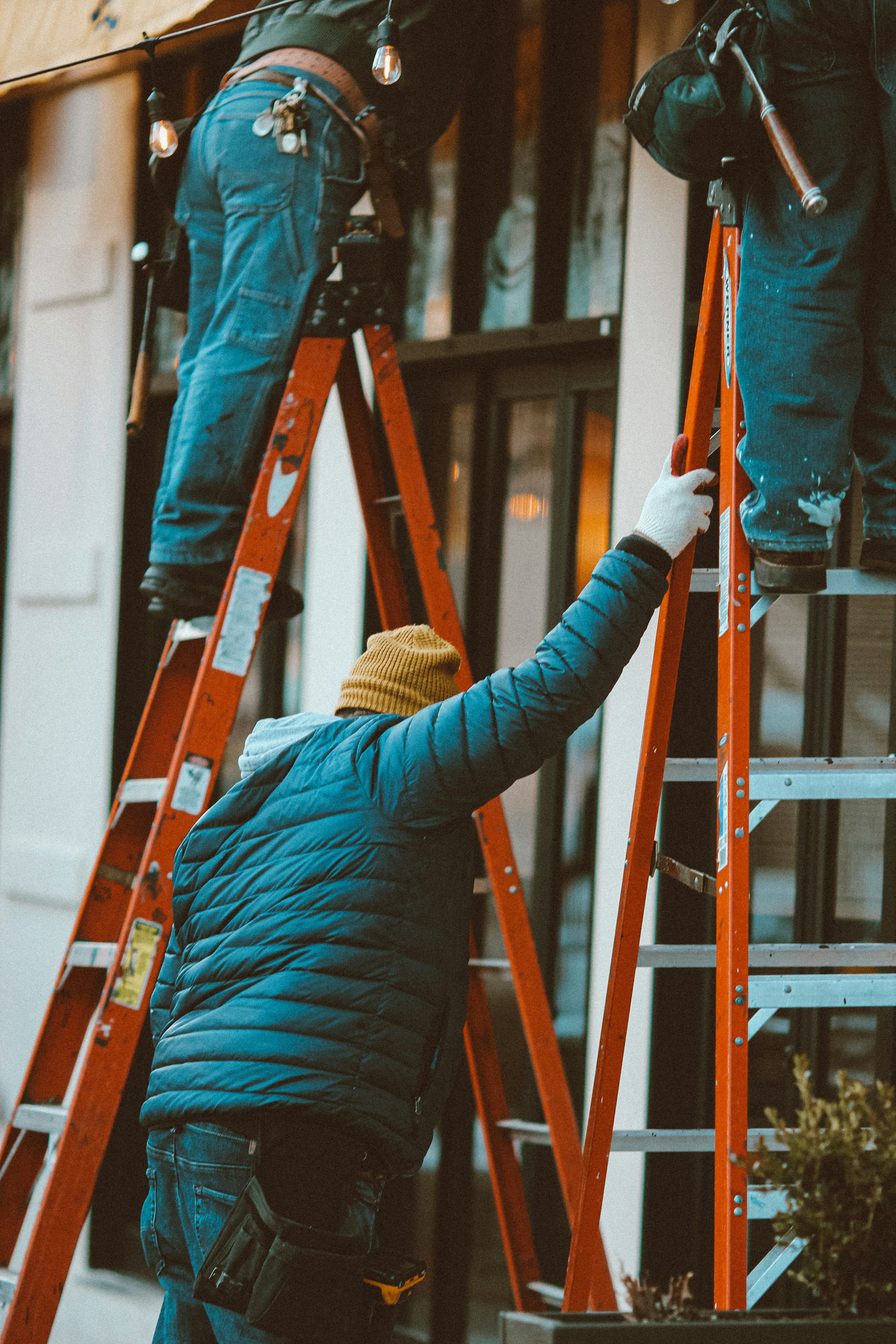 A team of tradespeople working together on ladders outside a building